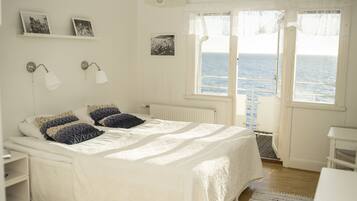 A bedroom with a bed, bedside tables, a nightstand, a window with a view of the sea, and wall-mounted picture frames.