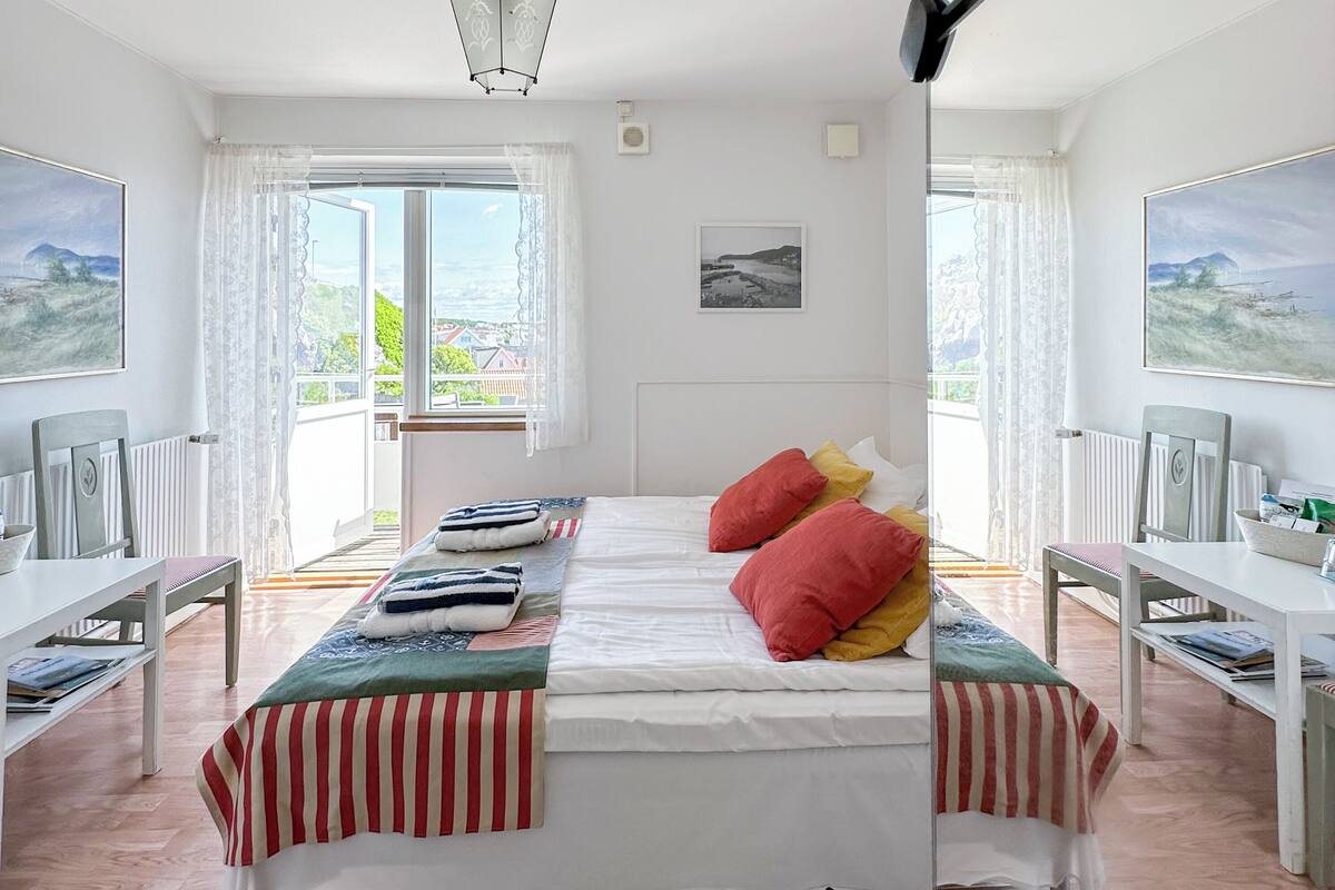 A bedroom with a large bed, two bedside tables, a window with curtains, and a view of the outside.