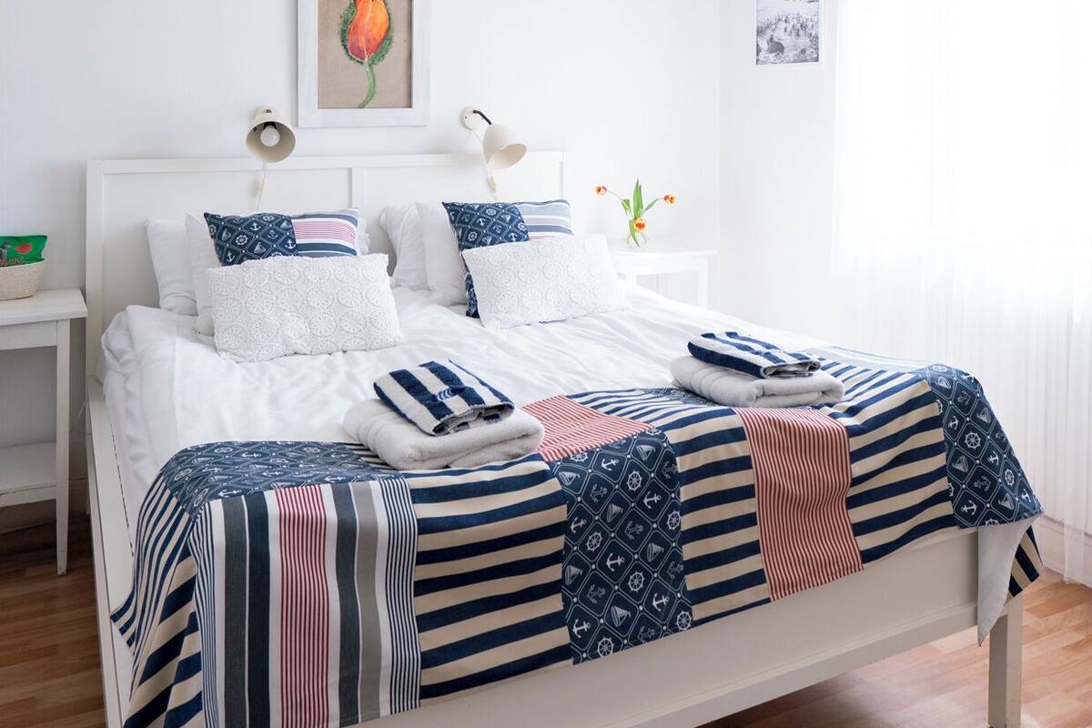 A neatly made bed with striped bedding, a white headboard, and a bedside table with a lamp.