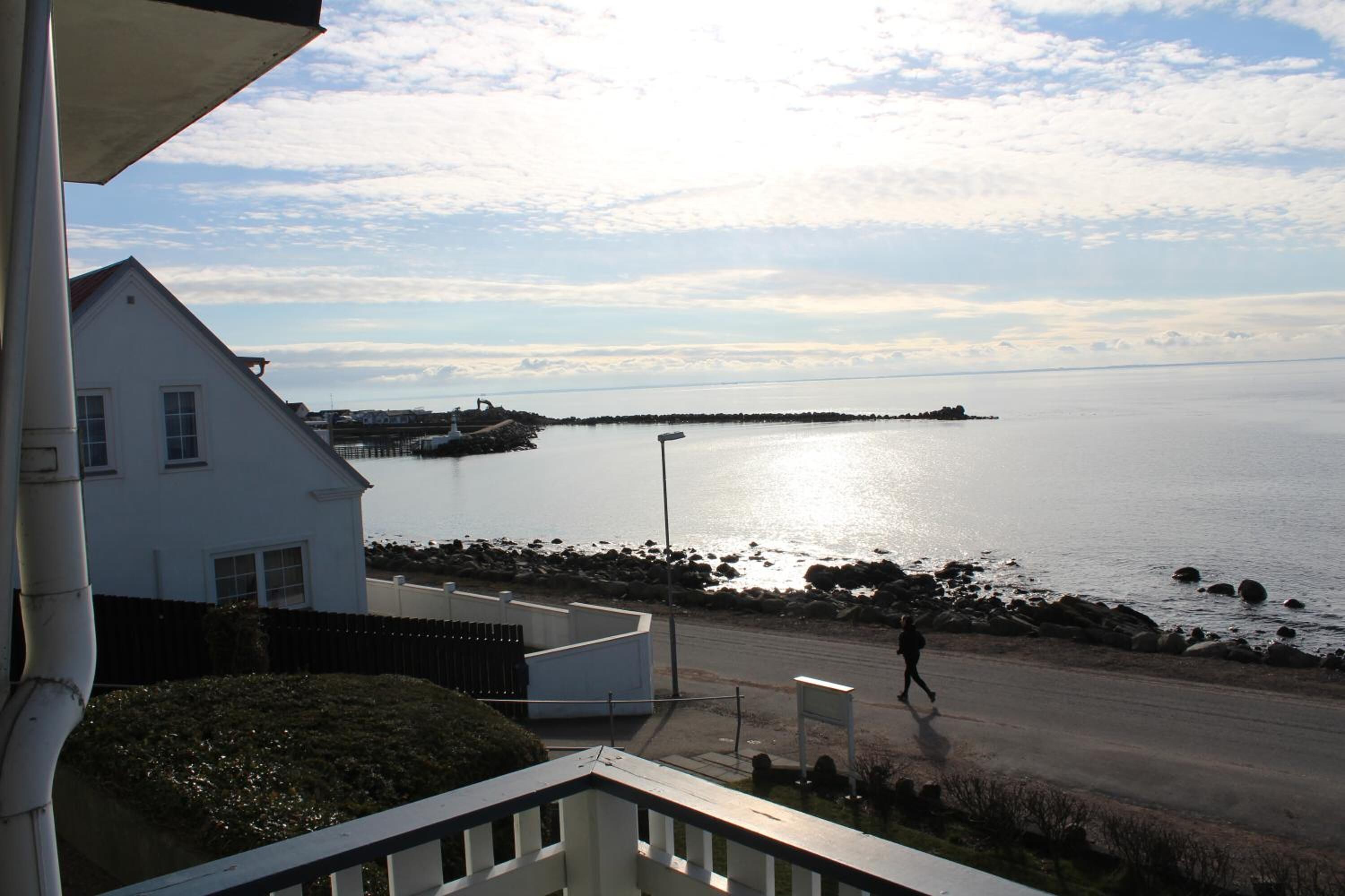 Vista costeira com uma casa, uma estrada e uma pessoa caminhando.