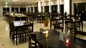 Un restaurante amplio con varias mesas y sillas, una zona de bar central y ventanas grandes.