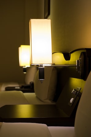 A hotel room interior with a bed, bedside tables, and a lamp.