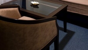 Una habitación con una mesa de vidrio, una silla de cuero marrón, un sofá beige y una alfombra azul.