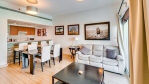 Ein modernes Wohnzimmer mit Essbereich, einer Couch und einem Couchtisch. An den Wänden befinden sich Bilder in Rahmen und ein Fenster mit Vorhängen.