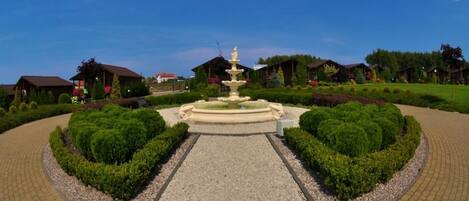 A landscaped garden with a central fountain, surrounded by neatly trimmed hedges and a gravel path.
