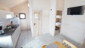 A compact room with a kitchenette, a bed, a TV, and a window. - Duet Domki (Postomino)