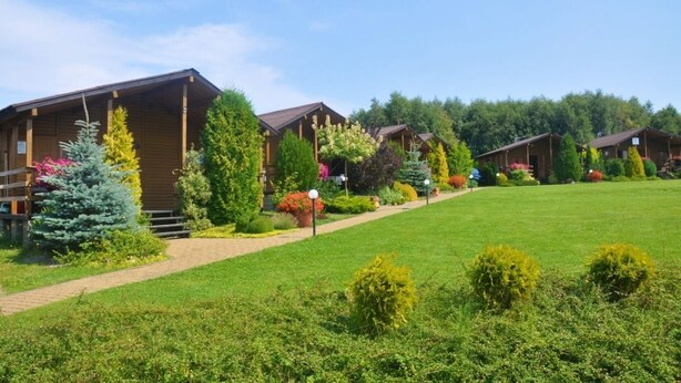 A row of wooden cabins with a well-maintained lawn and various shrubs and flowers. - Duet Domki (Postomino)