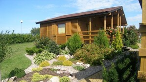 A wooden cabin with a balcony, surrounded by a landscaped garden with various plants and a paved pathway. - Duet Domki (Postomino)