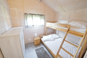 A small, wooden-paneled room with bunk beds, a bedside table with a lamp, and a window with curtains. - Duet Domki (Postomino)