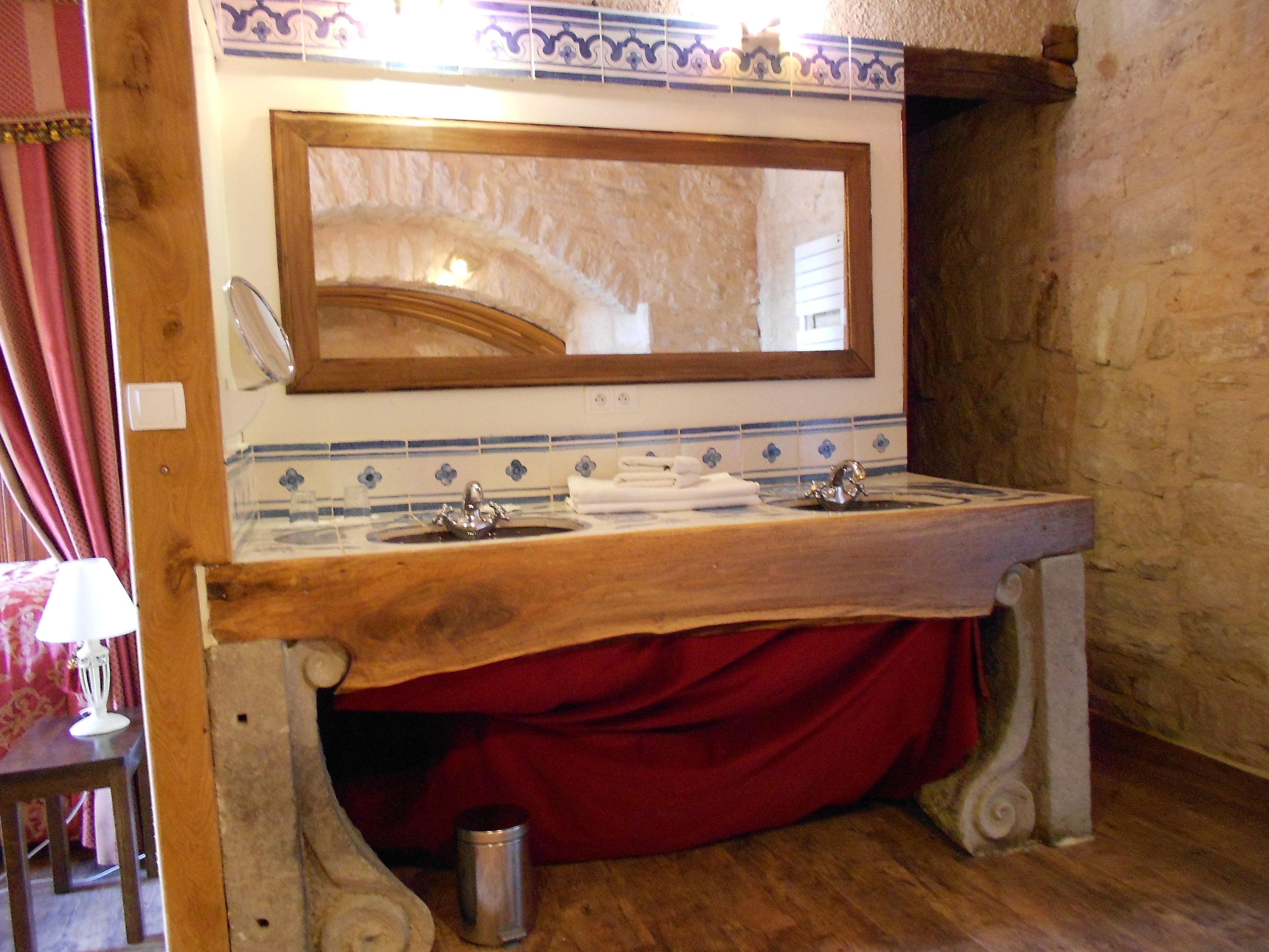 A bathroom with a wooden vanity, a large mirror, and a red bath mat.
