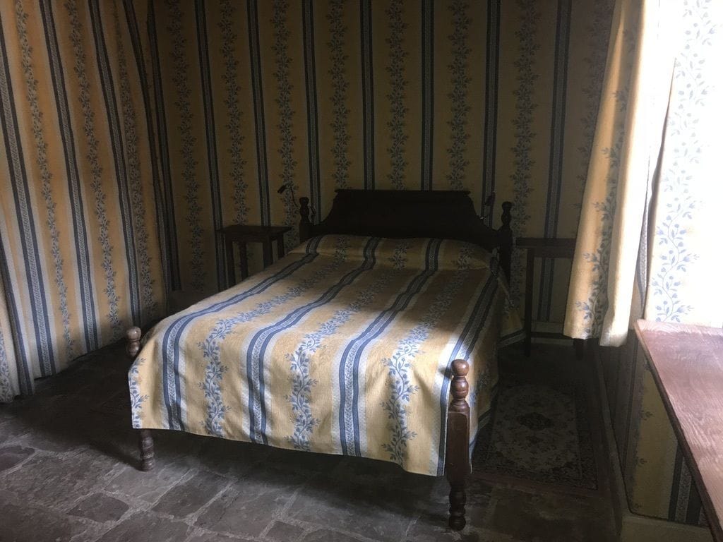 Una cama con colcha a rayas en una habitación con papel tapiz a rayas y una alfombra estampada.