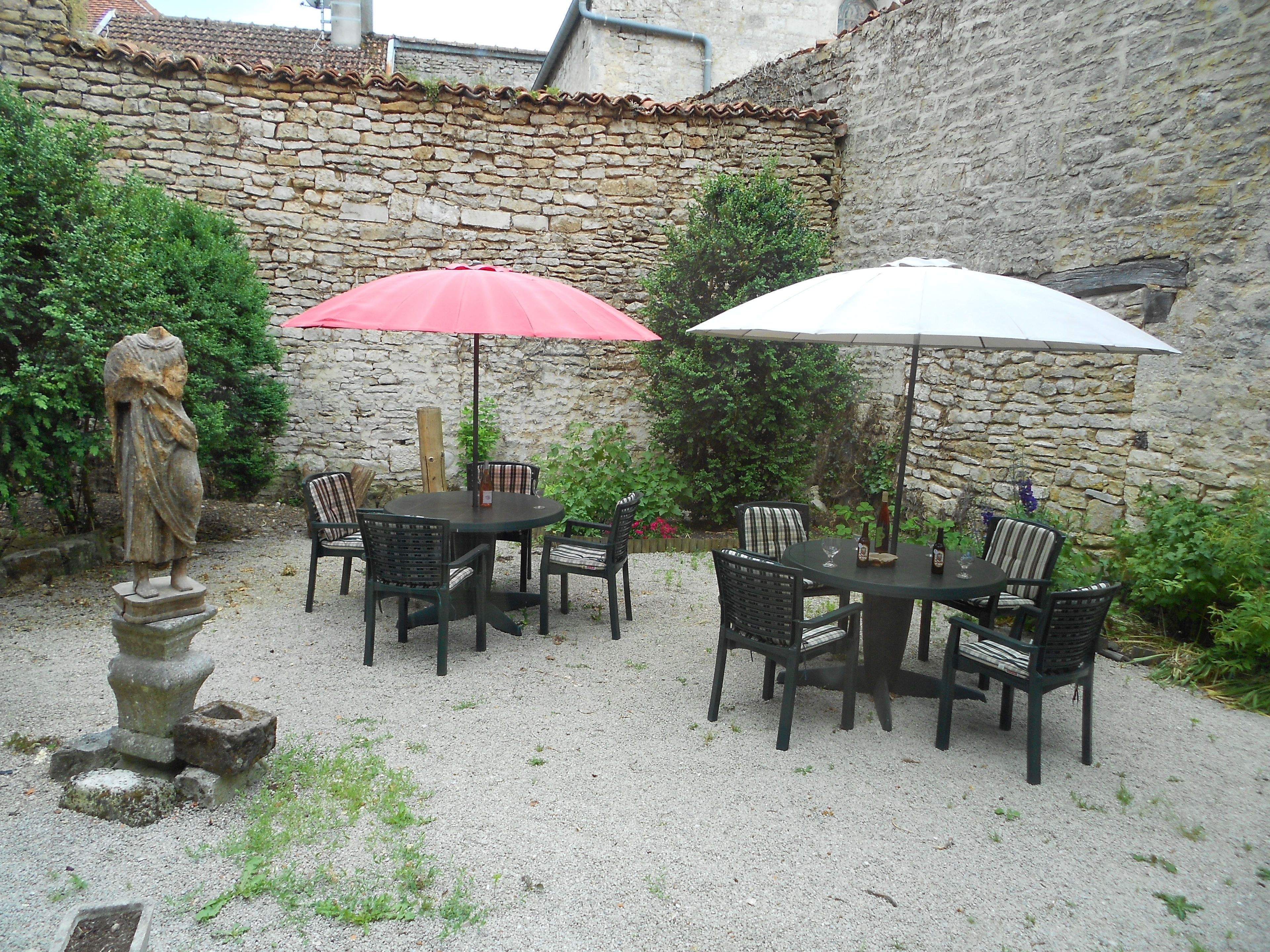 An outdoor patio with stone walls, two round tables with umbrellas, and wicker chairs.