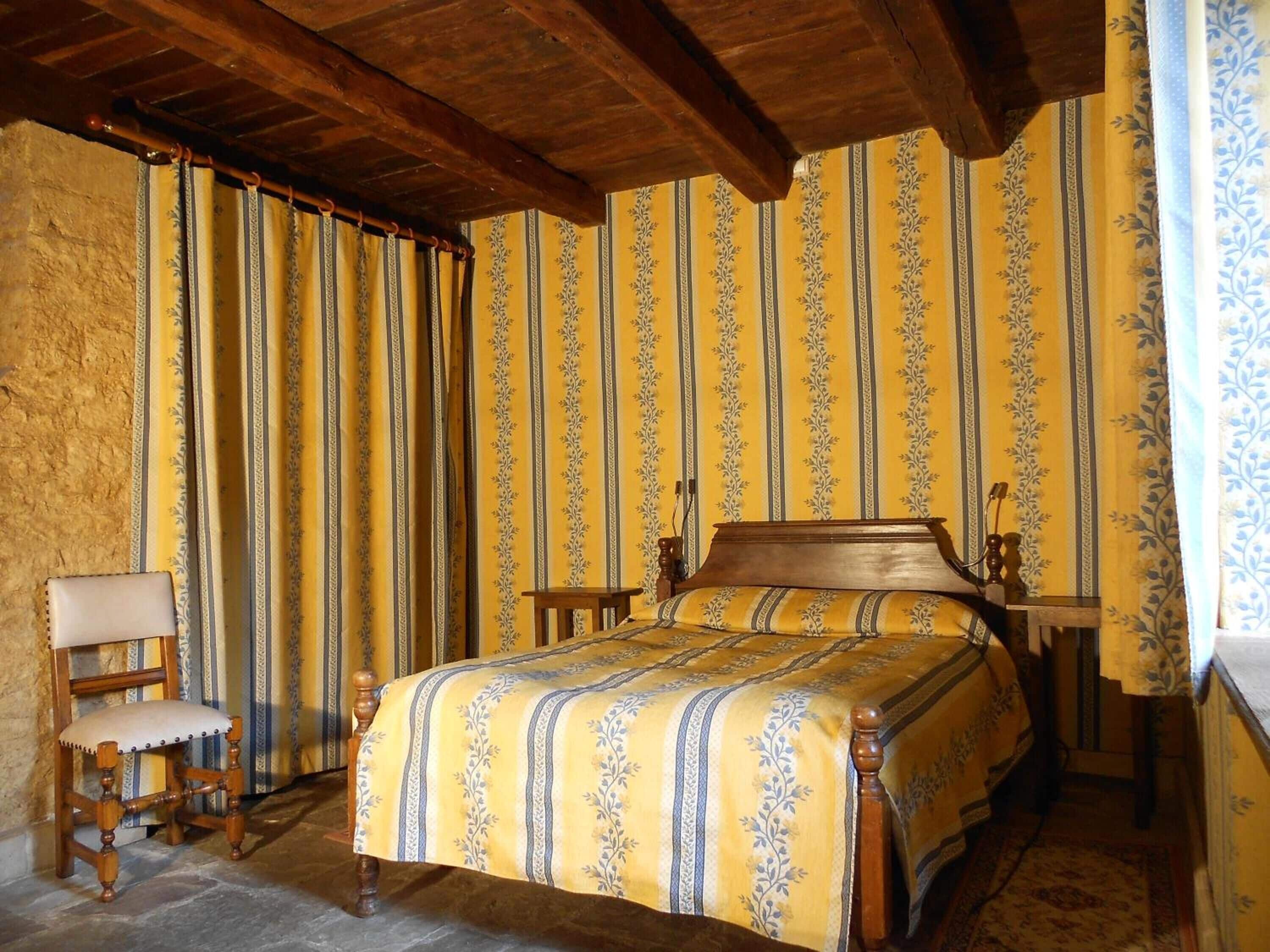 A bedroom with a wooden bed, a chair, and curtains with a floral pattern.