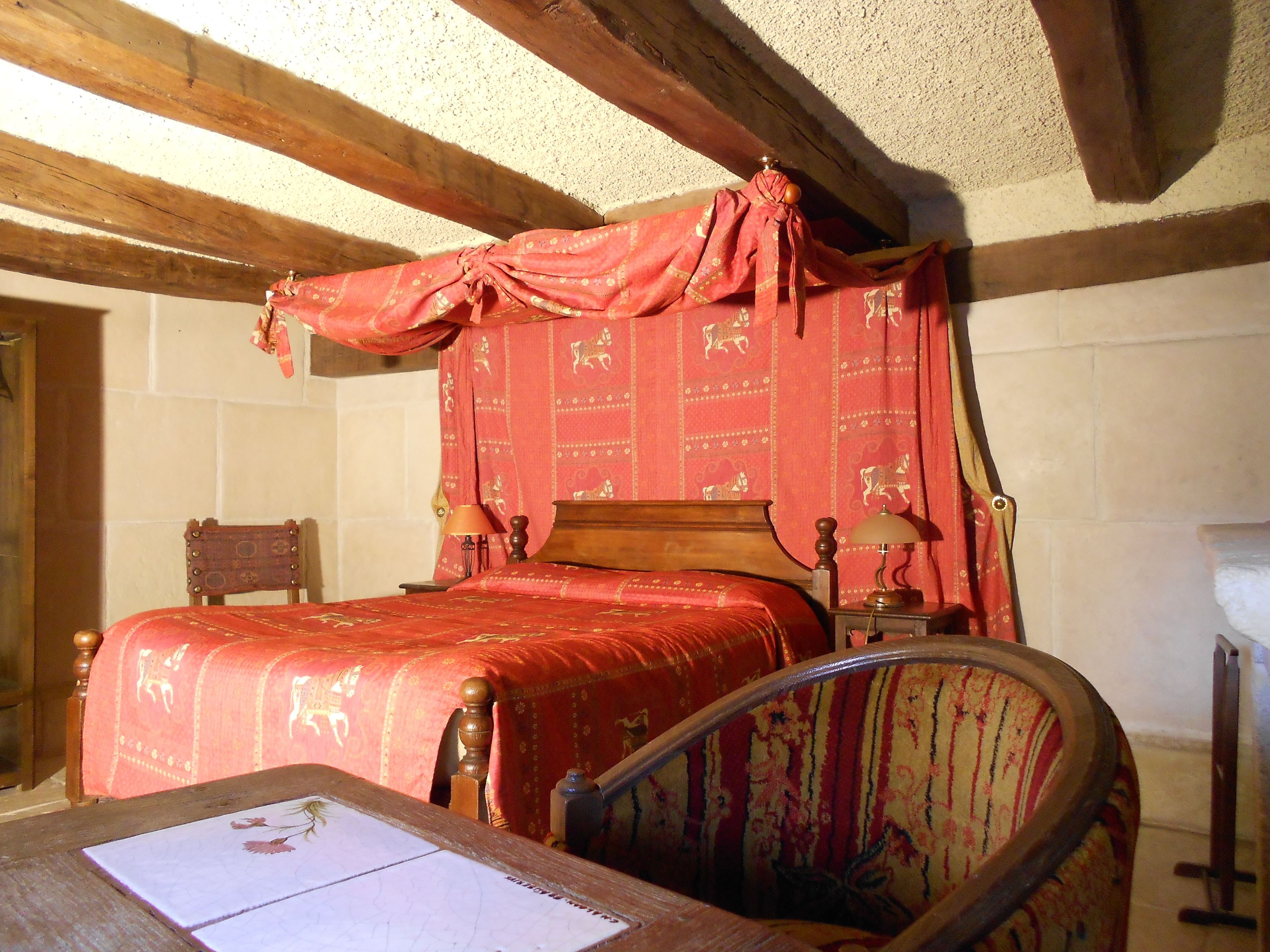 A traditional bedroom with a wooden bed, a chair, and a table with a book.