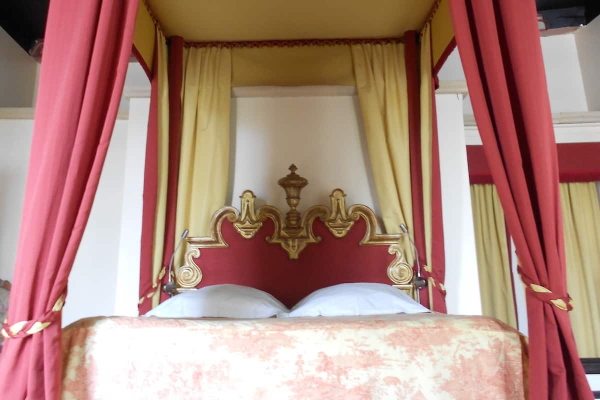 A four-poster canopy bed with a red and gold design, a white headboard, and red curtains.