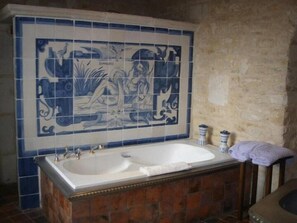 Un baño con una bañera grande, un lavamanos y una pared decorada con azulejos.