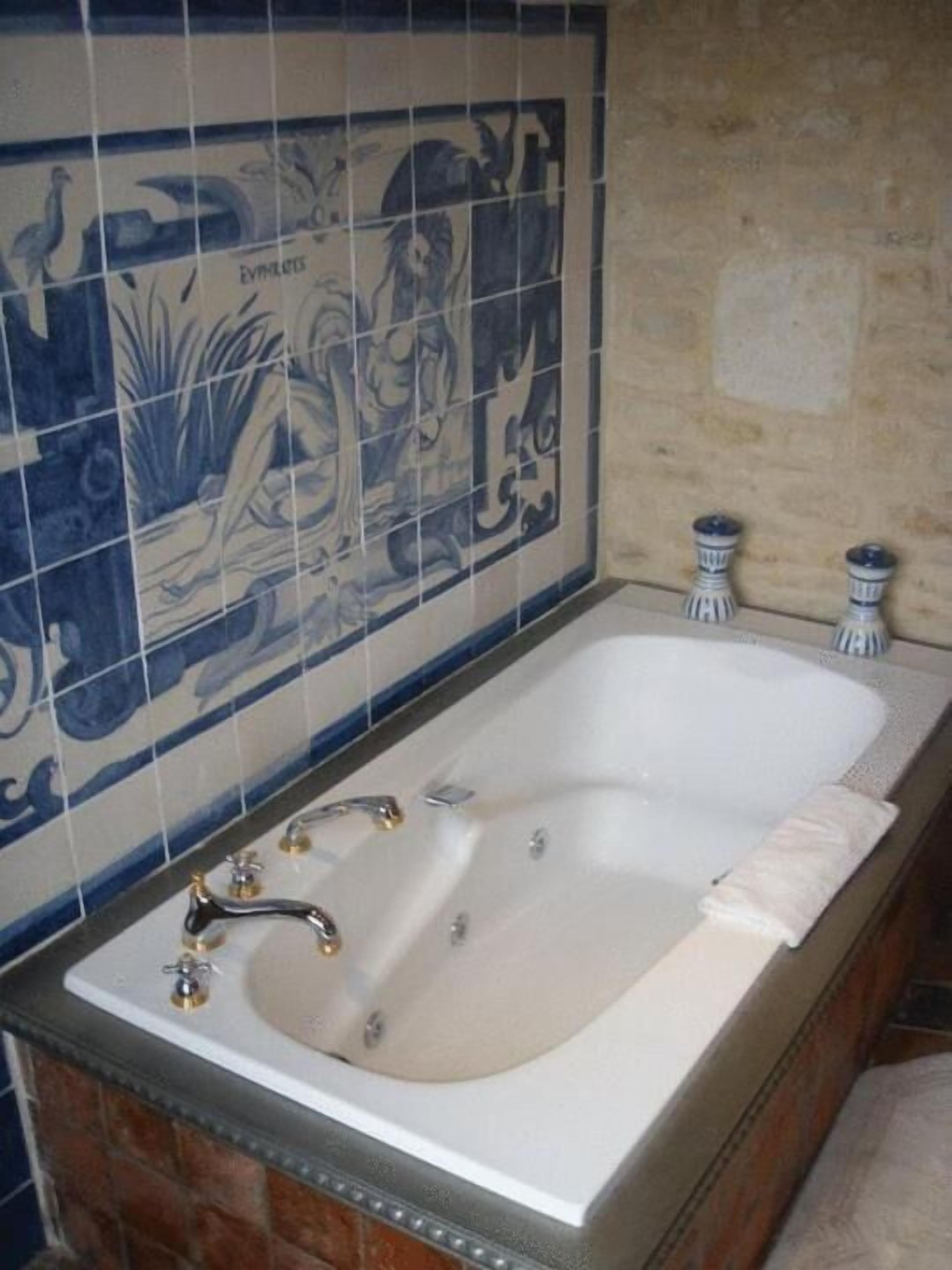 A bathroom with a white bathtub, a blue and white tiled wall, and a brick wall.