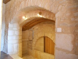 Un baño con paredes de piedra, un arco de madera, una ducha y un banco.