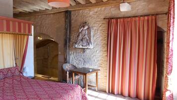 Een landelijke kamer met een stenen muur, een bed met een bedovertrek met dessin, een houten tafel en een stoel.