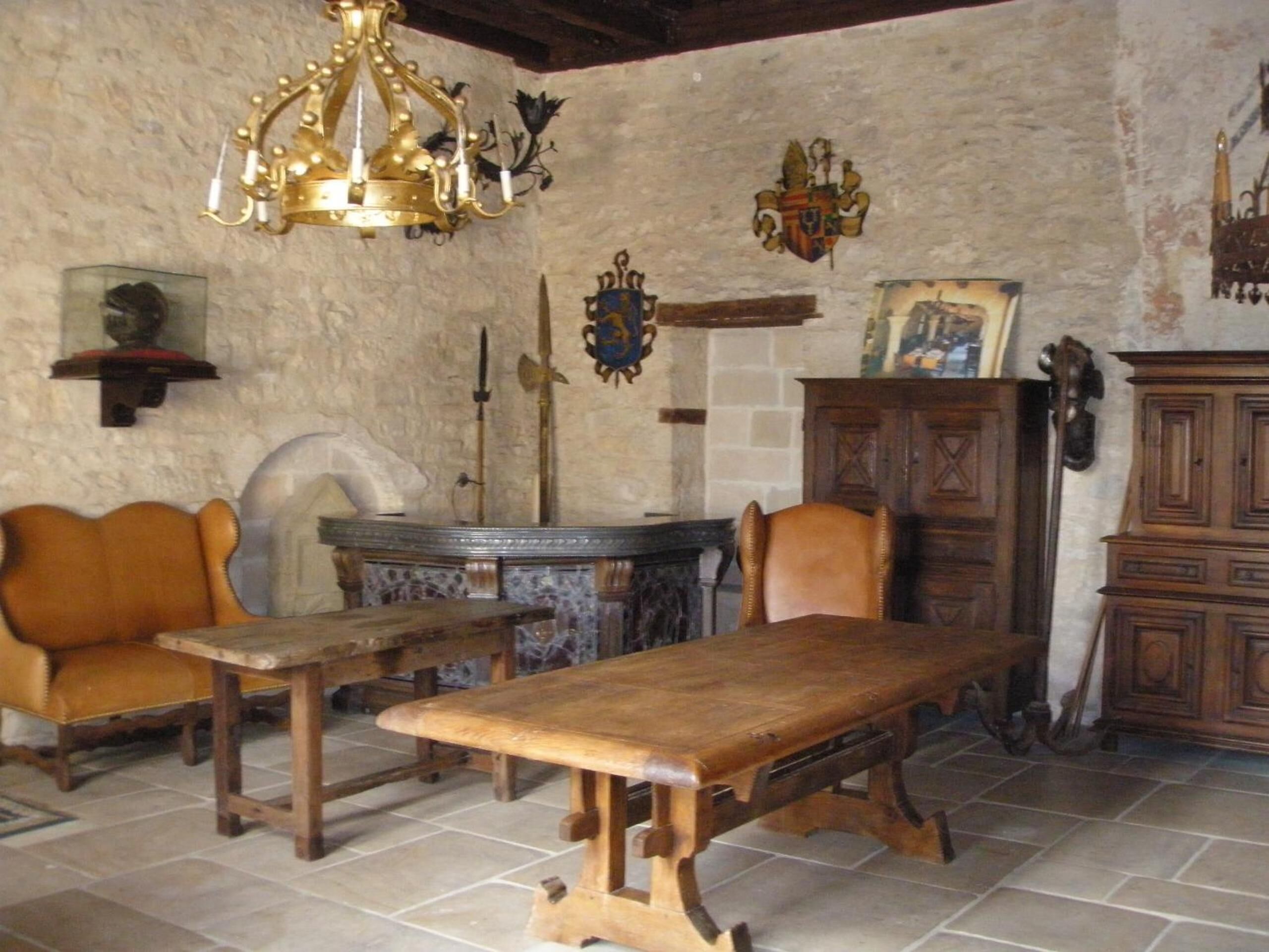 A rustic room with a wooden table, leather chairs, a chandelier, and a stone wall.