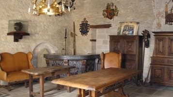 A rustic room with a wooden table, leather chairs, a chandelier, and a stone wall.