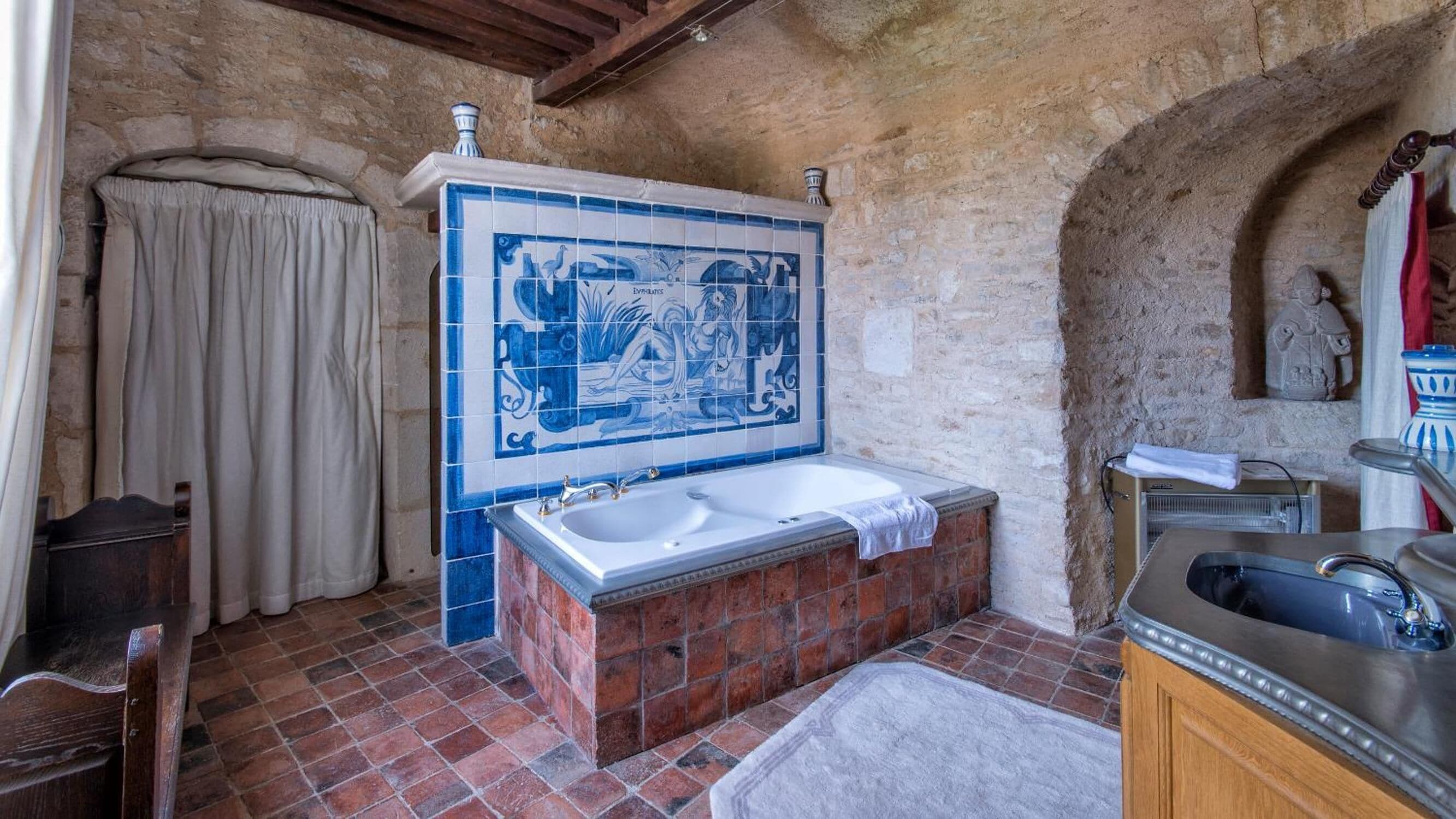A bathroom with a large bathtub, a tiled wall with a blue and white design, and a stone wall.
