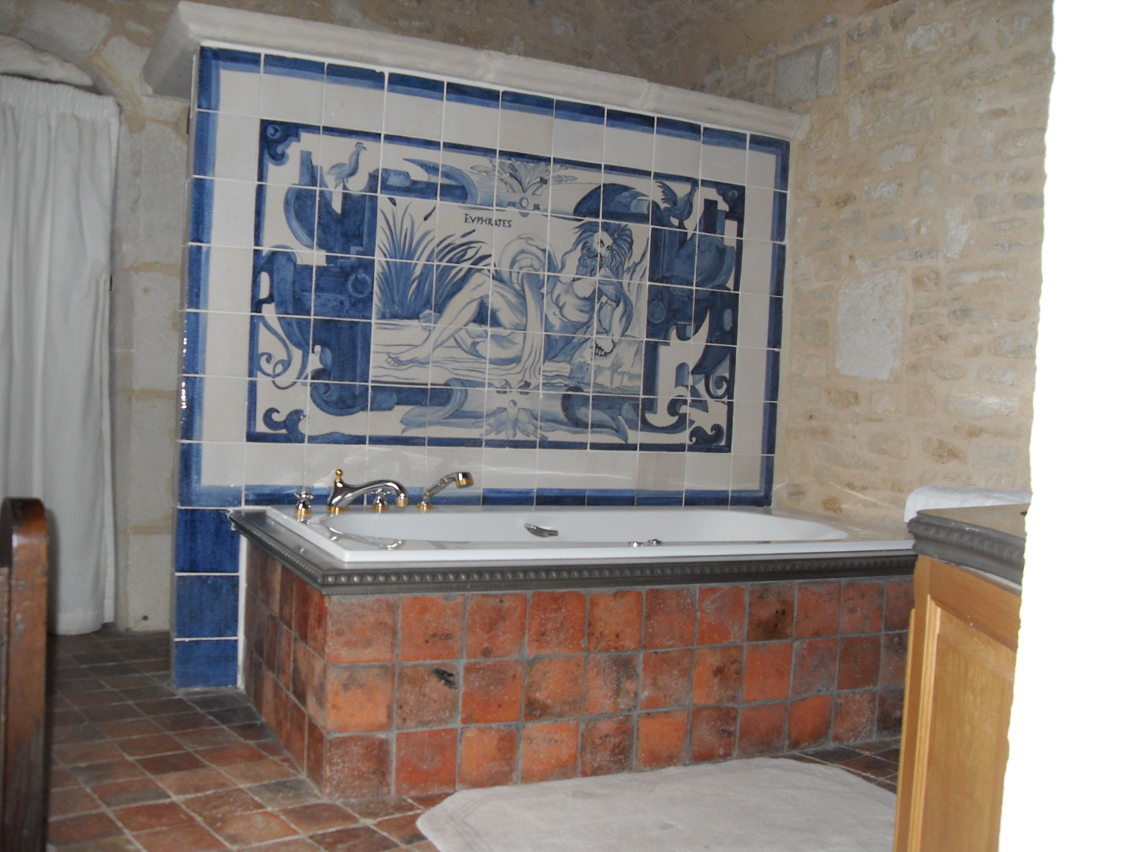 A bathroom with a bathtub, a tiled wall with a decorative design, and a stone wall.