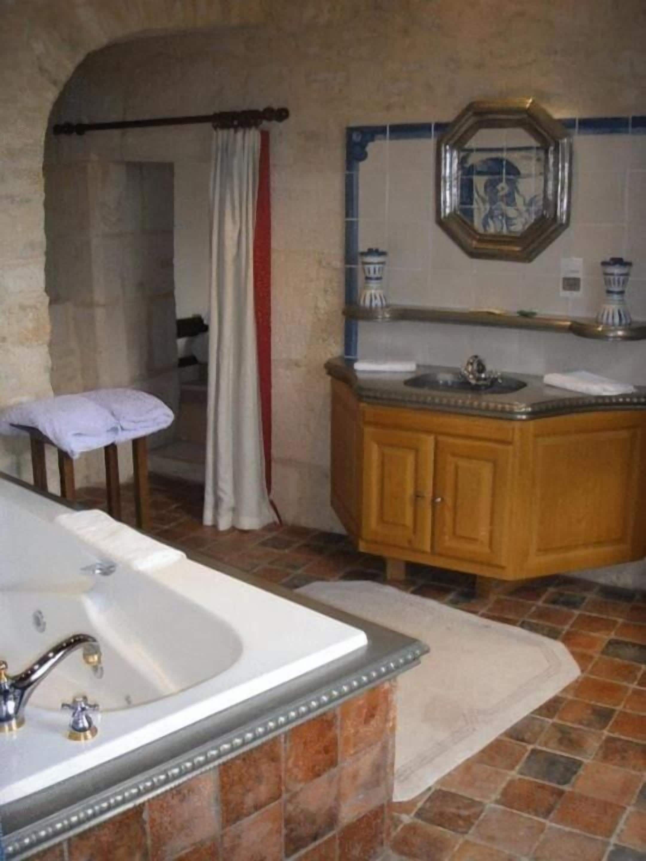 A bathroom with a bathtub, a wooden vanity, a mirror, and a tiled floor.