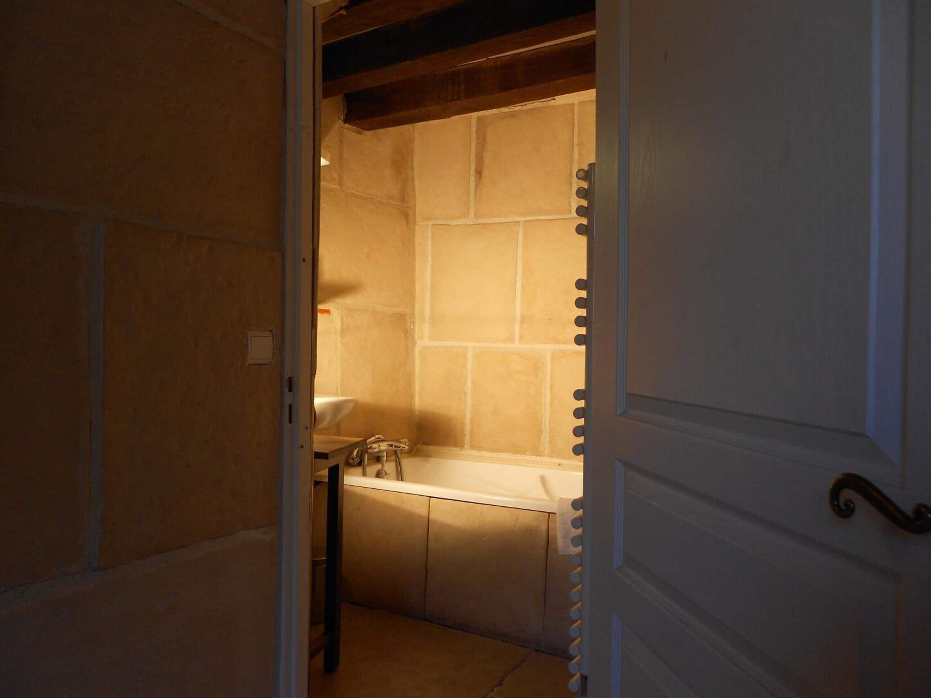Un couloir étroit mène à une salle de bain équipée d’un lavabo blanc et d’une baignoire.