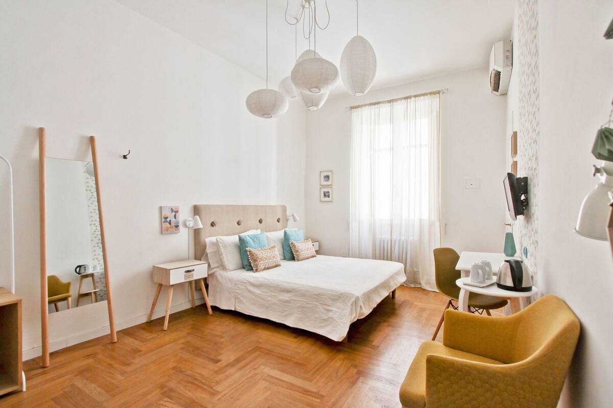 A bedroom with a bed, bedside table, chair, and a mirror.