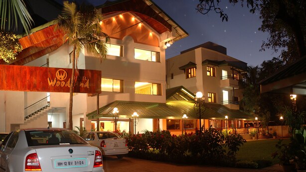 A hotel with a modern design, featuring a prominent sign, multiple levels, and a well-lit entrance. - Hotel Woodland (Kolhapur)