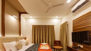 A hotel room with a bed, a TV, a ceiling fan, and a wooden wall unit. - Hotel Woodland (Kolhapur)