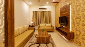 A living room with a sofa, a coffee table, a TV, and a patterned wall. - Hotel Woodland (Kolhapur)