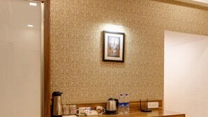 A hotel room with a wooden desk, a small refrigerator, a kettle, a coffee maker, and a framed picture on the wall. - Hotel Woodland (Kolhapur)