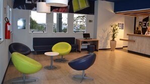 A modern reception area with a reception desk, a computer, and a seating area with colorful chairs. - ibis budget Divinopolis (Divinopolis)