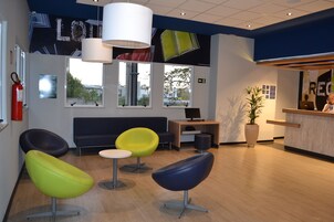 Uma área de recepção moderna com balcão, computador e espaço de espera com cadeiras coloridas.