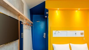 A hotel room with a bed, a blue door, a wooden shelf, and a white wall-mounted light fixture. - ibis budget Divinopolis (Divinopolis)