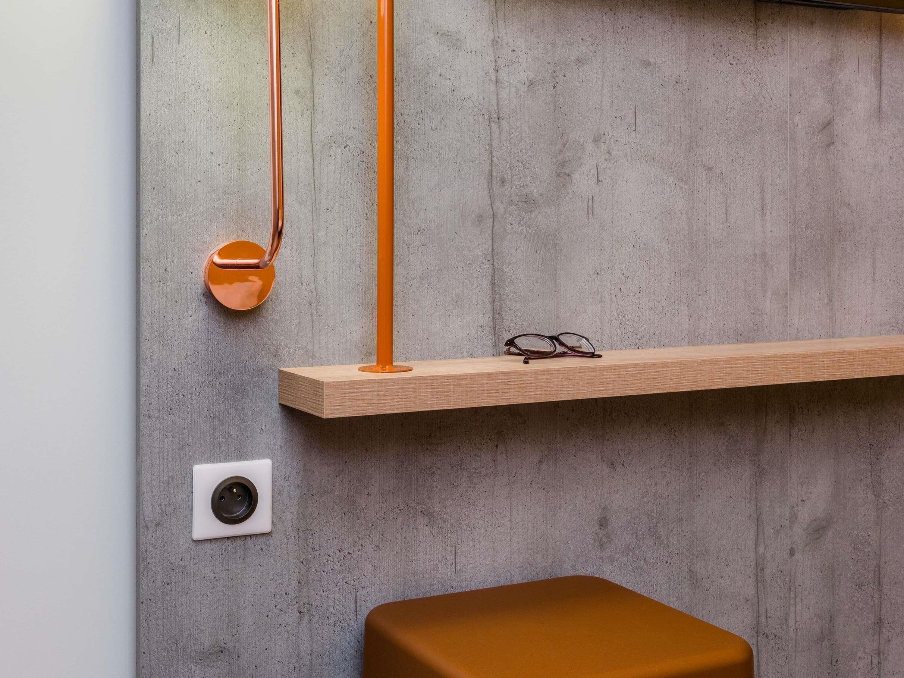 A minimalist room with a concrete wall, a wooden shelf with glasses, and a brown bench.