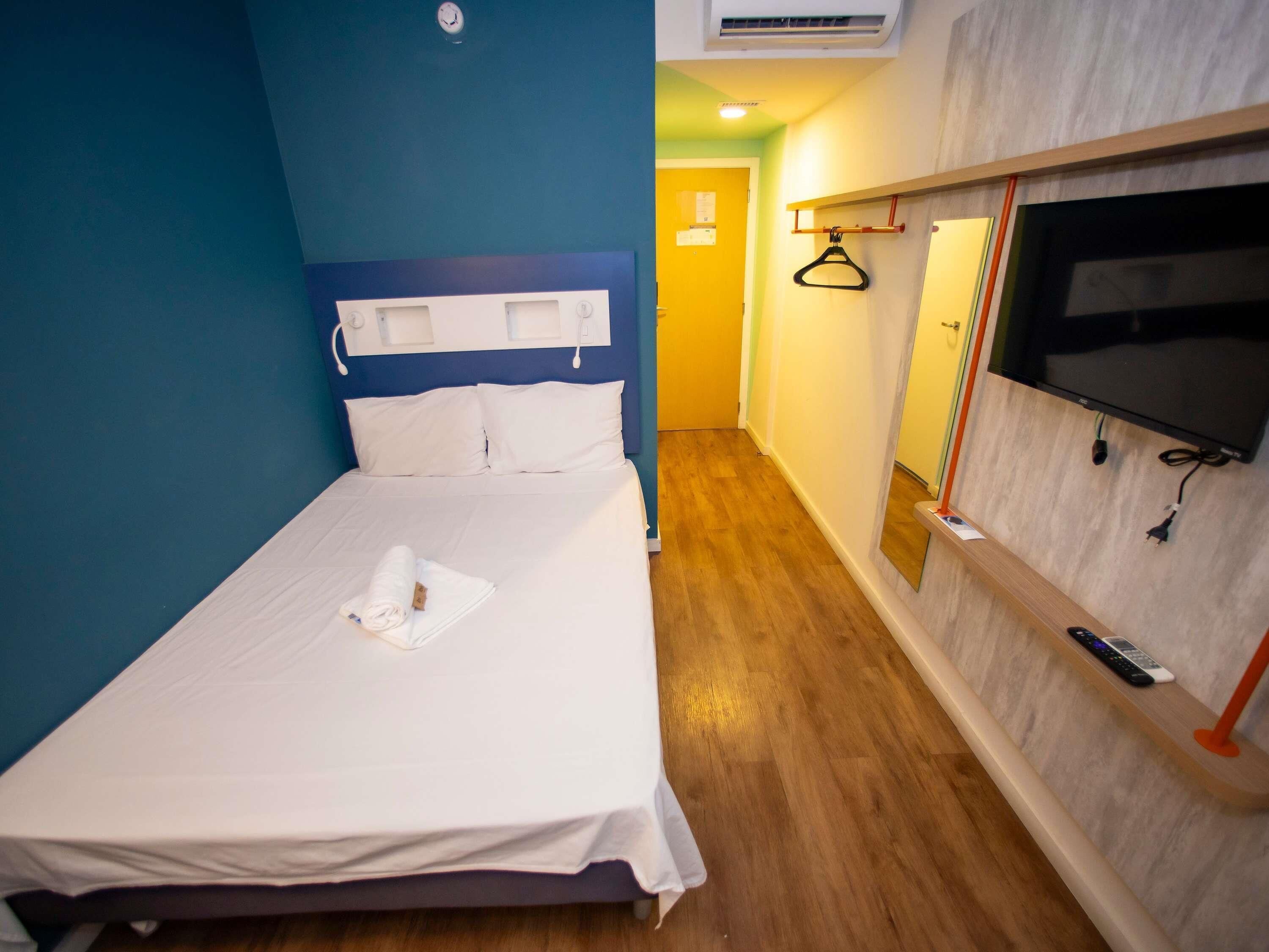 Habitación de hotel con cama, televisor montado en la pared y piso de madera.