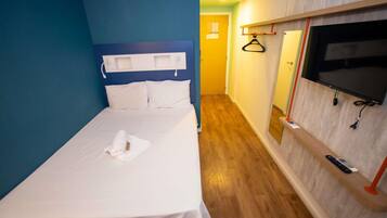 Habitación de hotel con cama, televisor montado en la pared y piso de madera.