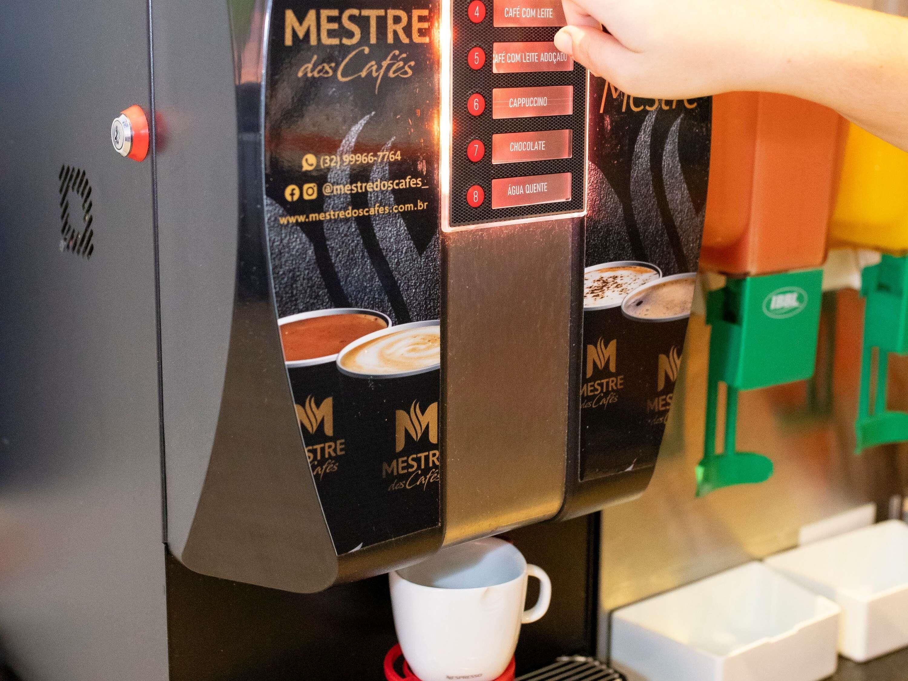 A coffee machine with a menu displaying options like 'CAFE COM LEITE' and 'CHOCOLATE.'