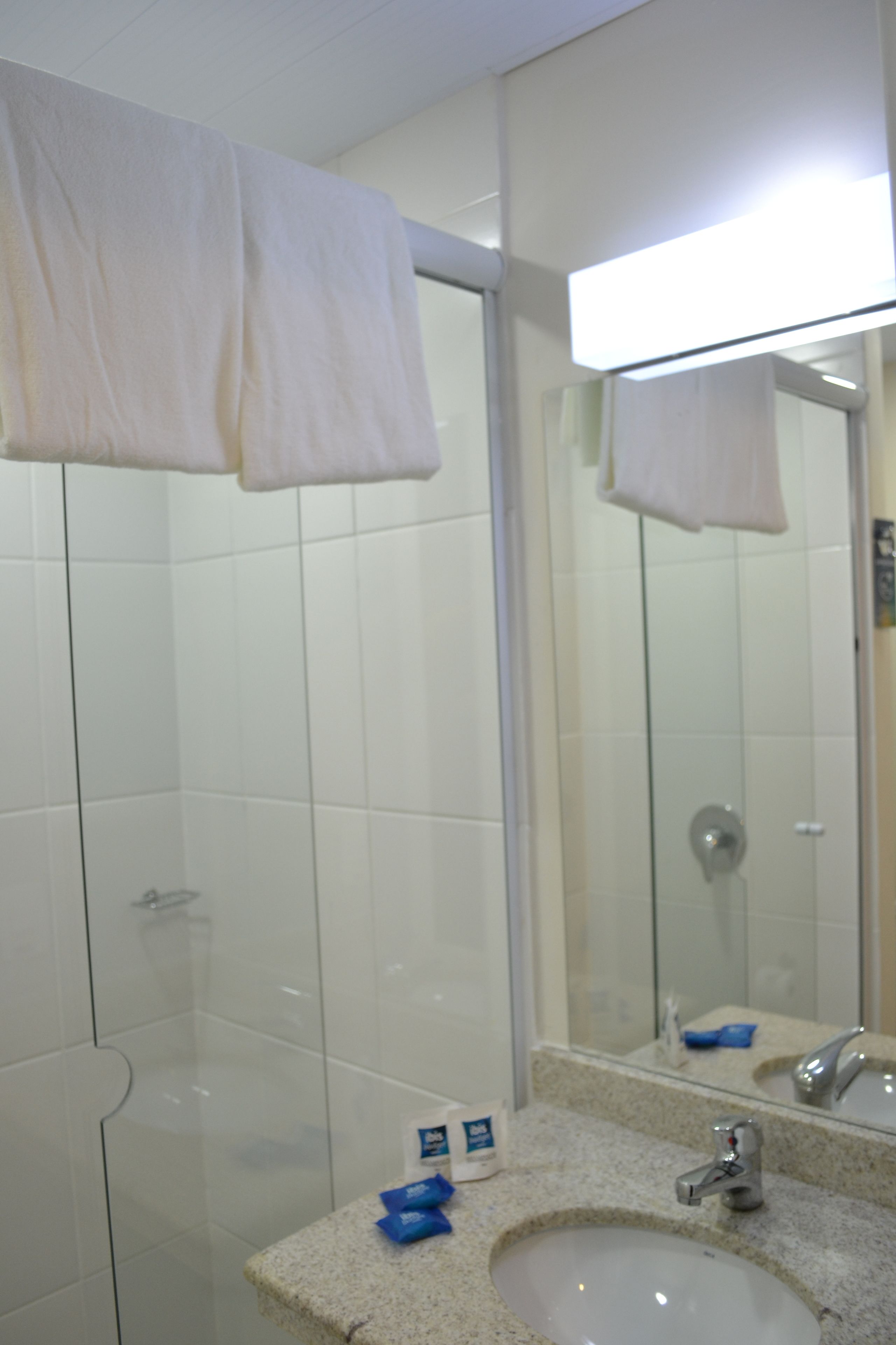 Un baño con cabina de ducha de vidrio, un lavabo con espejo y toallas blancas colgadas en la pared.