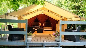 Un hébergement confortable en forme de tente, doté d'une terrasse en bois, de meubles en osier et d'un espace salon central.