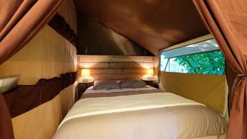 Een tentverblijf met een bed, twee bedlampen en uitzicht op groen.