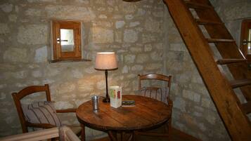 Una habitación rústica con paredes de piedra, una mesa de madera, sillas, una lámpara y una escalera.