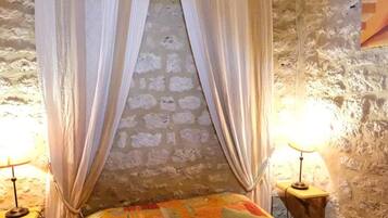 Un dormitorio rústico con techo de madera, pared de piedra, cama con colcha de colores y dos lámparas de noche.