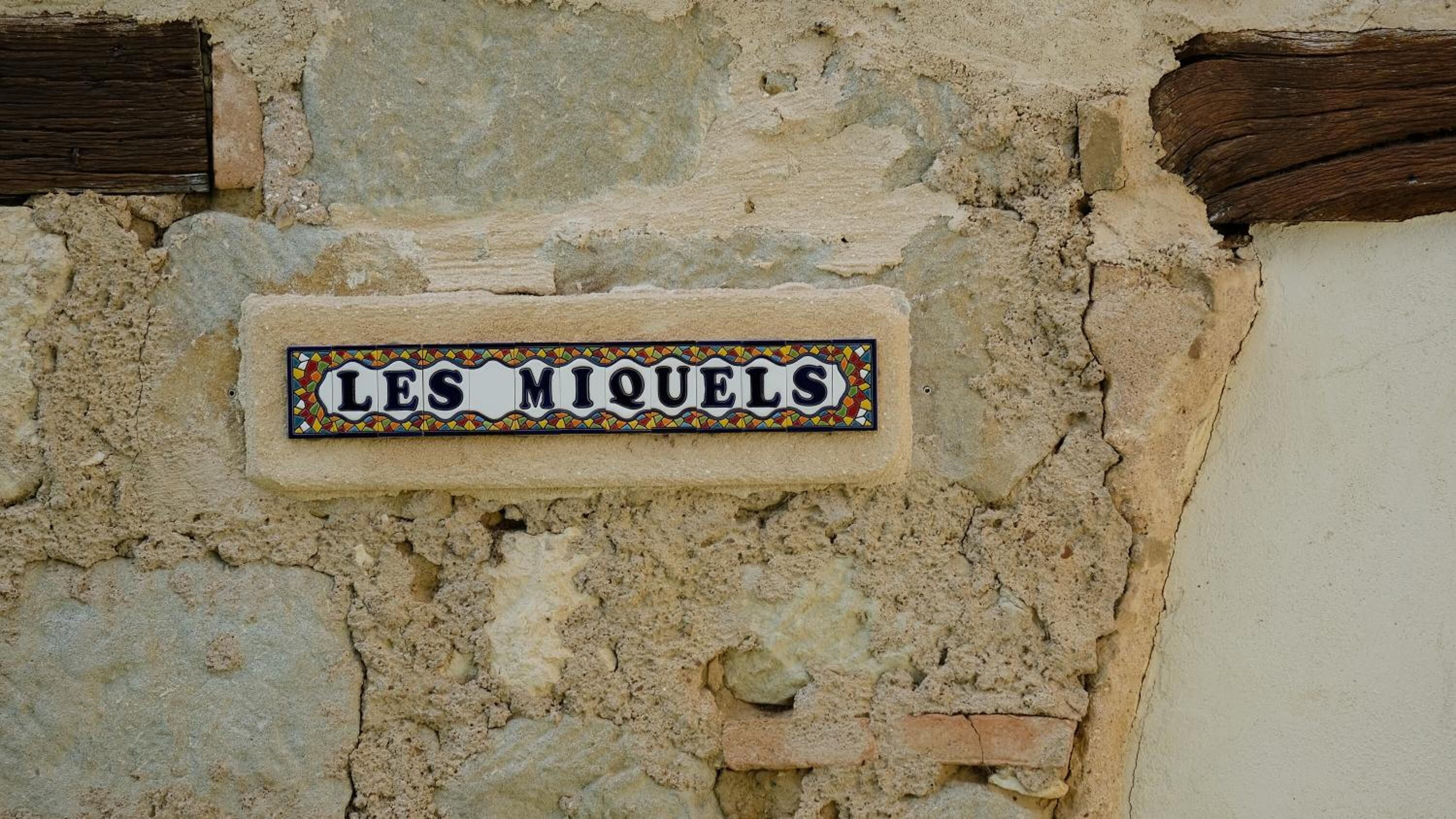 Un cartello con la scritta "LES MIQUELS" su un muro di pietra.