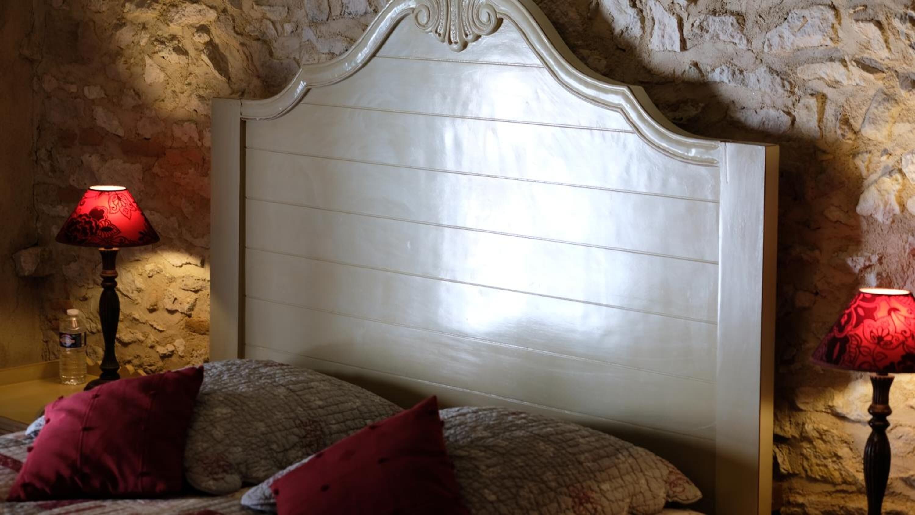 Ein Schlafzimmer mit Steinwand, weißem Kopfteil, zwei Nachttischlampen und roten Kissen.
