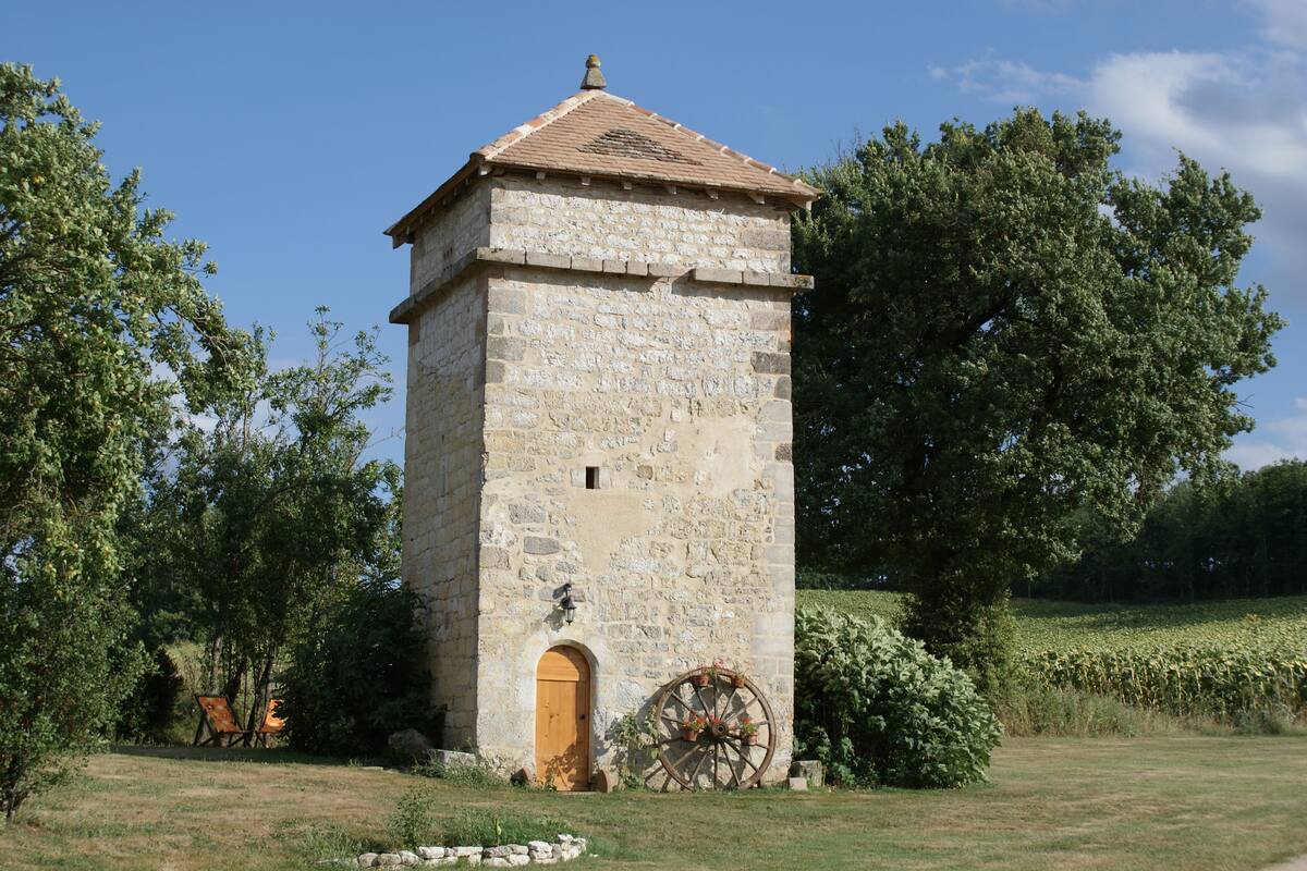 Une tour de pierre surmontée d’un toit en tuiles, dotée d’une entrée en arc de cercle et d’une grande roue en bois.