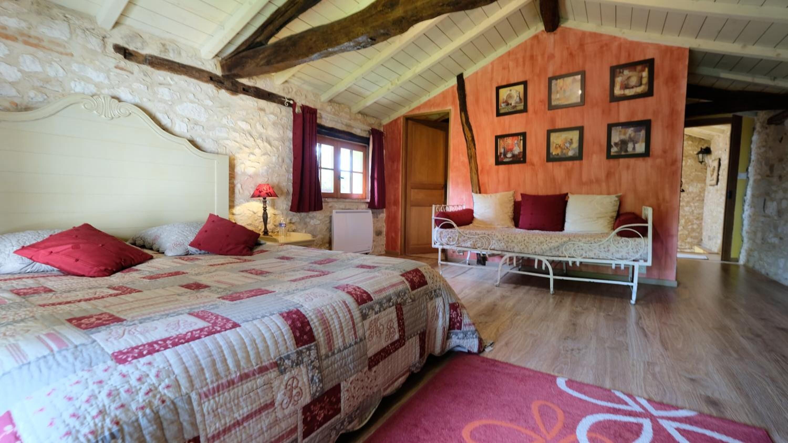 A bedroom with a large bed, a smaller sofa, a stone wall, and a wooden ceiling.